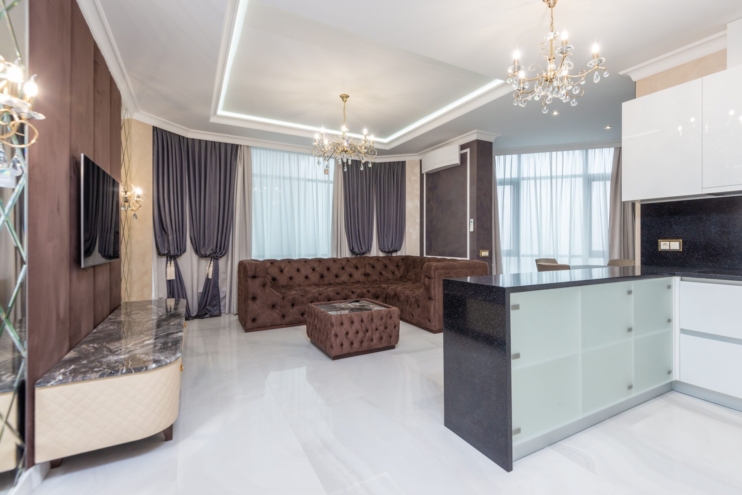 Spacious modern living room featuring elegant chandeliers, plush sofa, and contemporary decor.